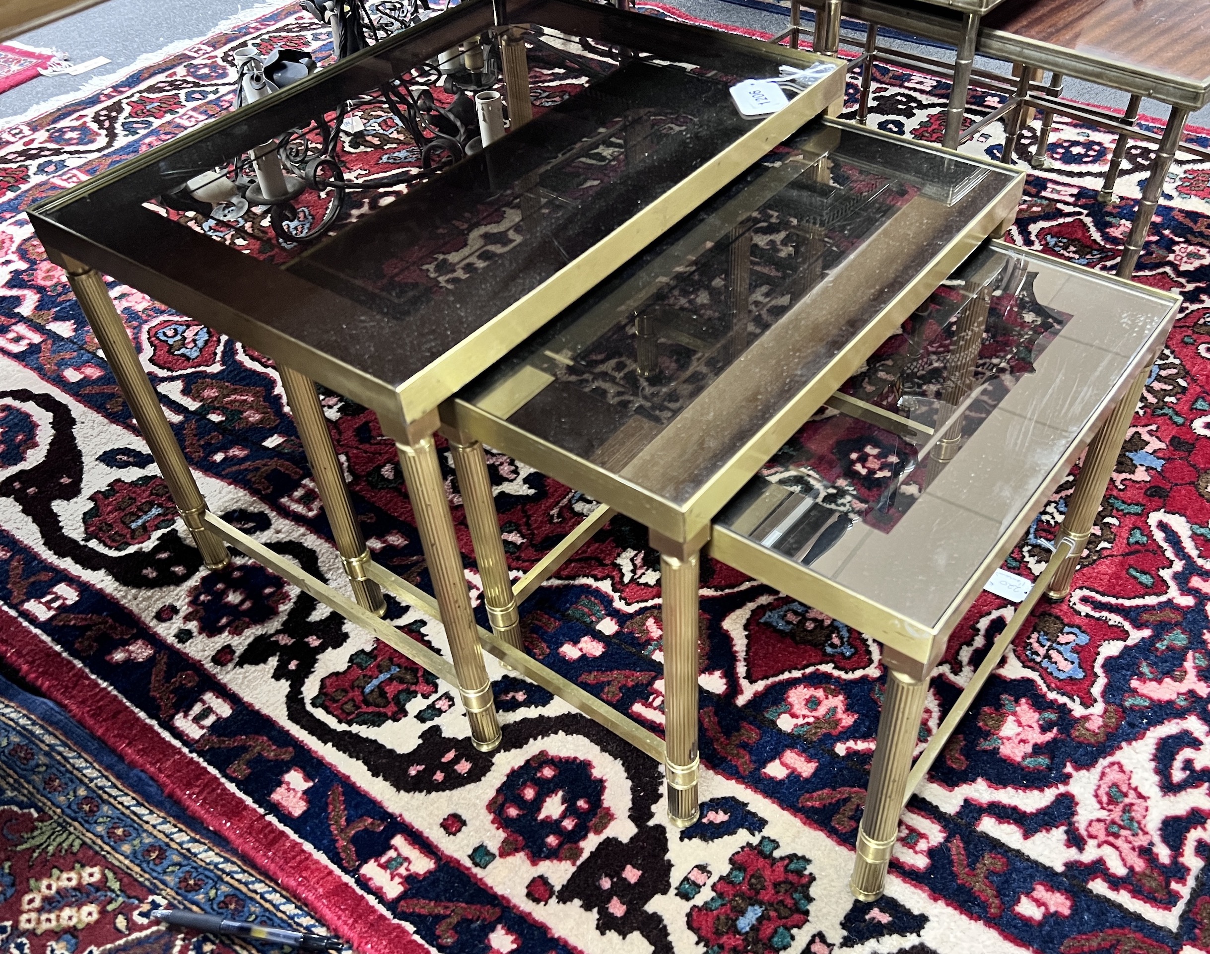 A nest of three 'Maison Charles' style brass and smoked glass topped tables, largest width 50cm